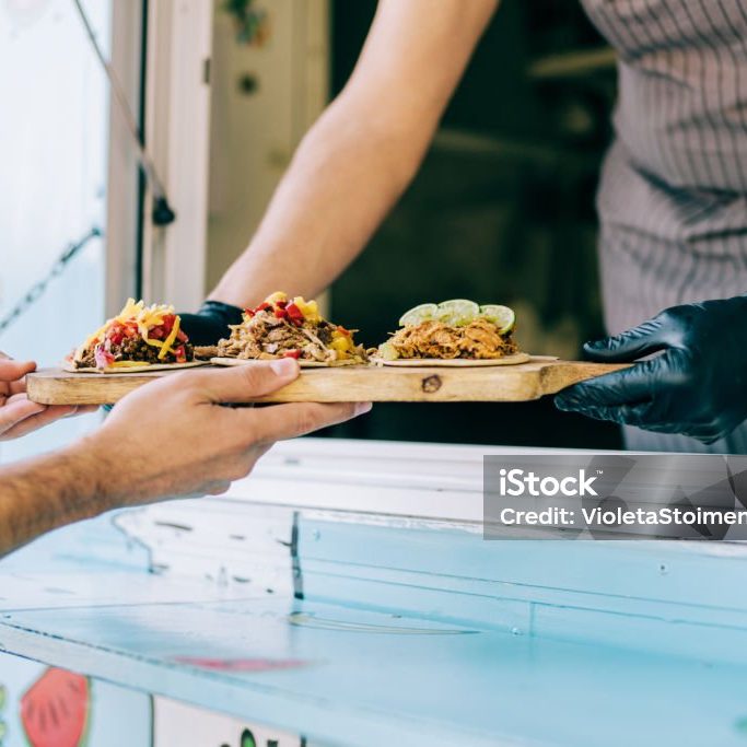 Cropped shot of young chef serving tasty tacos to male customer from the window of his food van.